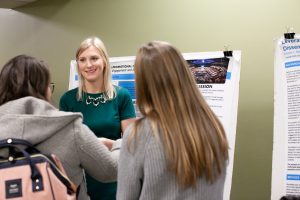 Student presents their research to multiple individuals in front of a research poster