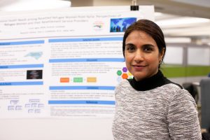 Student in front of a research poster, the text of which is blurred behind them.