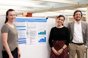 Students smile in front of a research poster, the text of which is not readable.