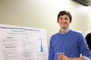 Student in front of a research poster. A partial title is visible: "...Multi-Product Firms with Cost Complementarities."