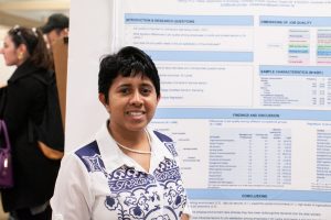 Student in front of a research poster. The text on the poster behind them is blurred.