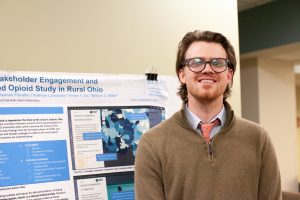 Student smiles in front of a research poster. The title is not fully visible.