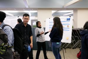 Student presenting their research in front of a research poster