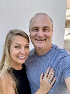 Photo of Rocky Riviella and his new fiance Carole smiling at the camera. Carole has her hand on Rocky's chest, showing off her new engagement ring.